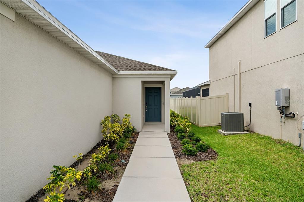 A concrete walkway leads to a dark blue front door between two beige houses — 6434 MILESTONE LOOP, PALMETTO, FL
