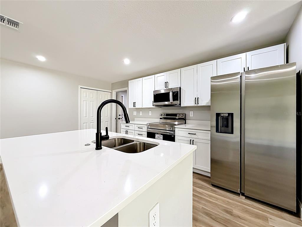A modern kitchen features white cabinets, stainless steel appliances, and a large white island — 6 CEDAR TRACE COURT, OCALA, FL