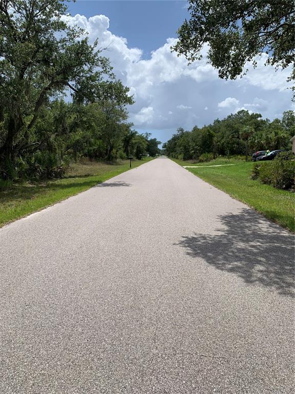 A paved residential street stretches into the distance, flanked by trees and grassy areas — 17496 BILLIAR AVENUE, PORT CHARLOTTE, FL