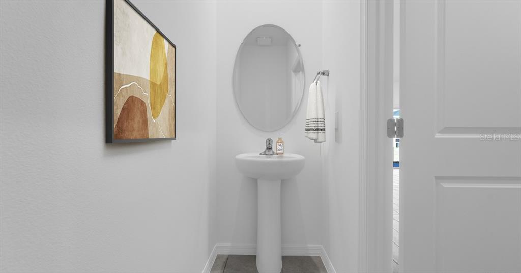 A small powder room features a white pedestal sink, an oval mirror, and abstract wall art — 10128 MORNING MEADOWLARK TRAIL, PARRISH, FL
