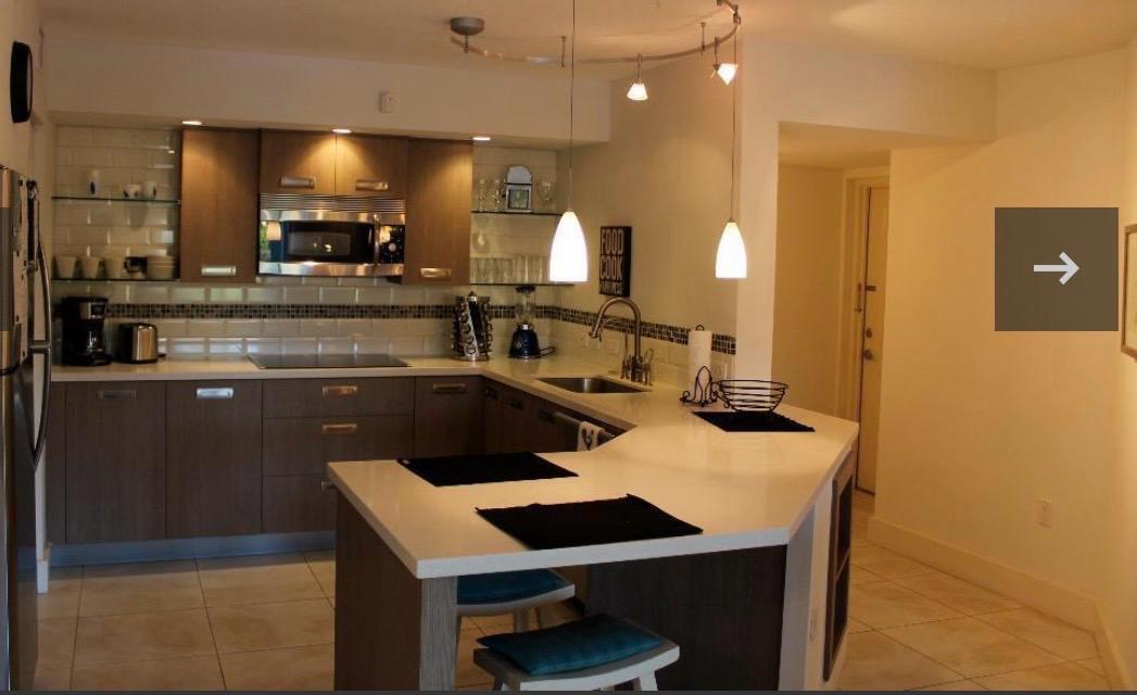 A modern kitchen features dark wood cabinets, white countertops, a breakfast bar, and pendant lighting — 808 Villa Circle, Boynton Beach FL 33435, BOYNTON BEACH, FL