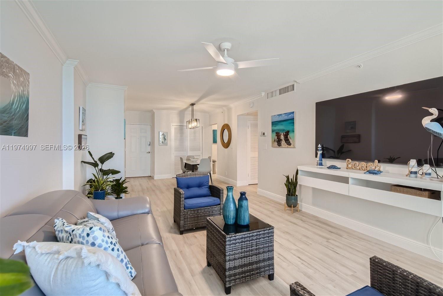 A living room features light wood-look flooring, a grey sofa, wicker chairs, and a television — 2501 S Ocean Dr, Hollywood FL 33019, HOLLYWOOD, FL