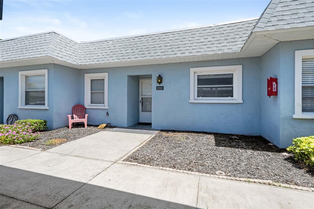 A light blue single-story building exterior features a concrete walkway, a red chair, and windows — 3534 TEESIDE DRIVE, NEW PORT RICHEY, FL