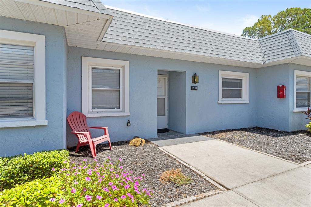 A light blue house exterior features a red chair, a walkway, and a front entrance — 3534 TEESIDE DRIVE, NEW PORT RICHEY, FL