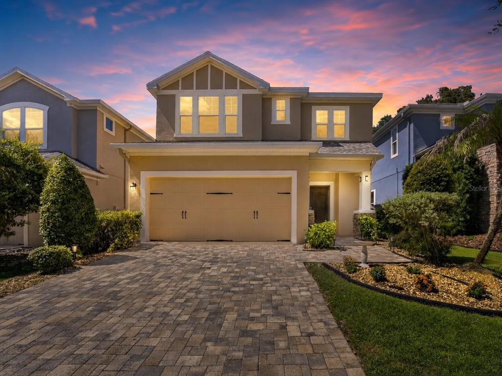 A two-story suburban house with a tan stucco exterior and a paved driveway at sunset — 16220 BAYBERRY VIEW DRIVE, LITHIA, FL