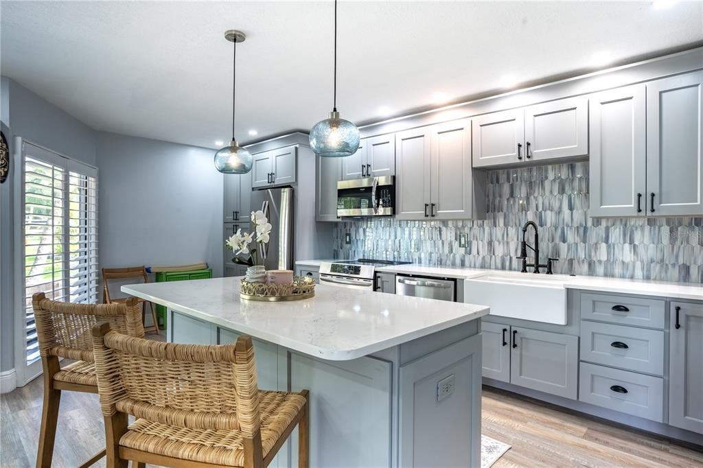 A kitchen features gray cabinets, a white quartz island, and a blue patterned tile backsplash — 1005 S BAYSHORE BOULEVARD UNIT 102, SAFETY HARBOR, FL