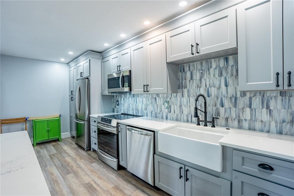 A modern kitchen features gray cabinets, stainless steel appliances, a farmhouse sink, and blue-toned backsplash — 1005 S BAYSHORE BOULEVARD UNIT 102, SAFETY HARBOR, FL