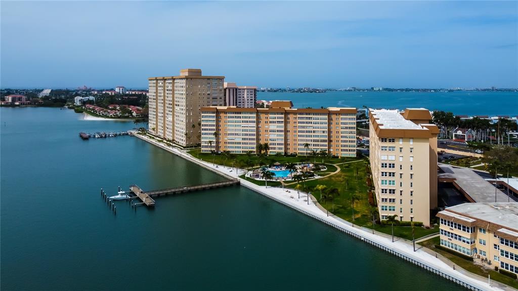 An aerial view shows waterfront apartment buildings with a swimming pool and a long pier — 5200 BRITTANY DRIVE S UNIT 204, ST PETERSBURG, FL