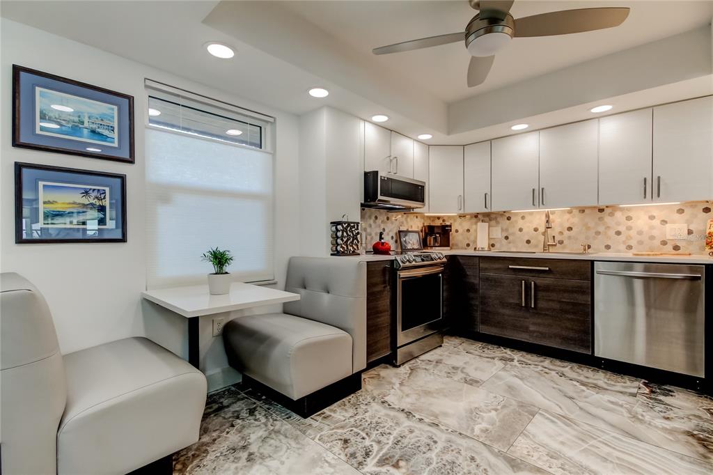 A kitchen features white upper cabinets, dark lower cabinets, stainless steel appliances, and a dining booth — 5200 BRITTANY DRIVE S UNIT 204, ST PETERSBURG, FL