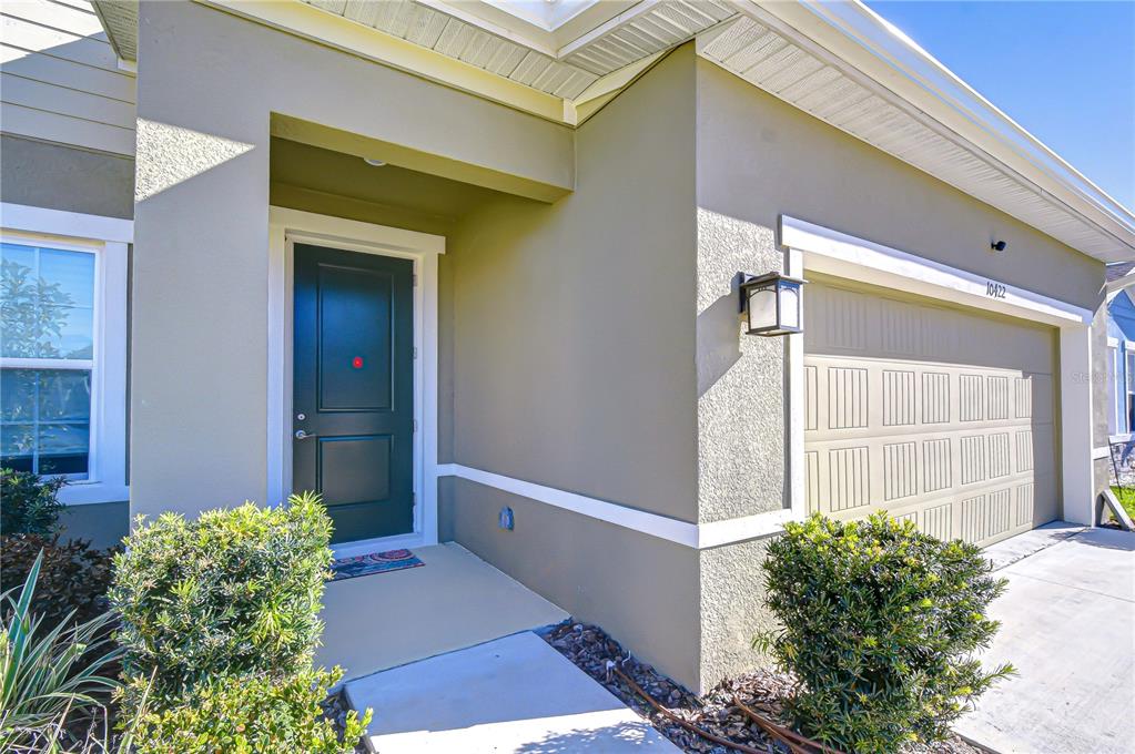 The exterior of a house features a dark front door and a two-car garage — 10422 GLIDING EAGLE WAY, LAND O LAKES, FL