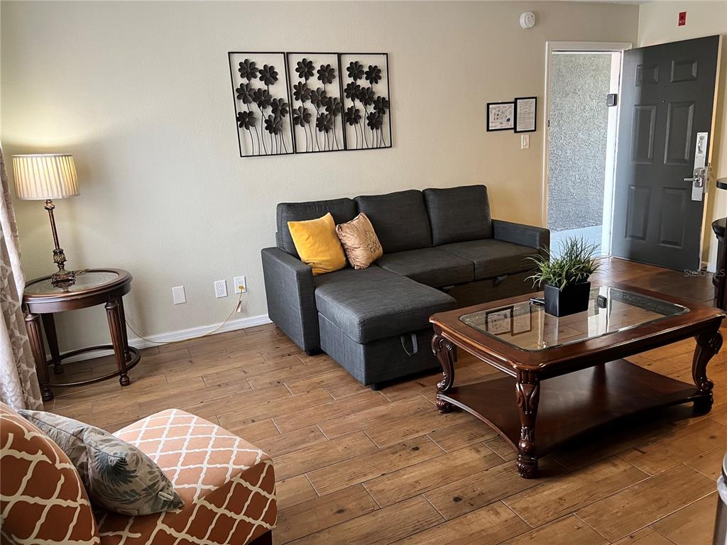 A living room features a gray sectional sofa, a glass-topped coffee table, and wood-look flooring — 3100 PARKWAY BOULEVARD UNIT 611, KISSIMMEE, FL
