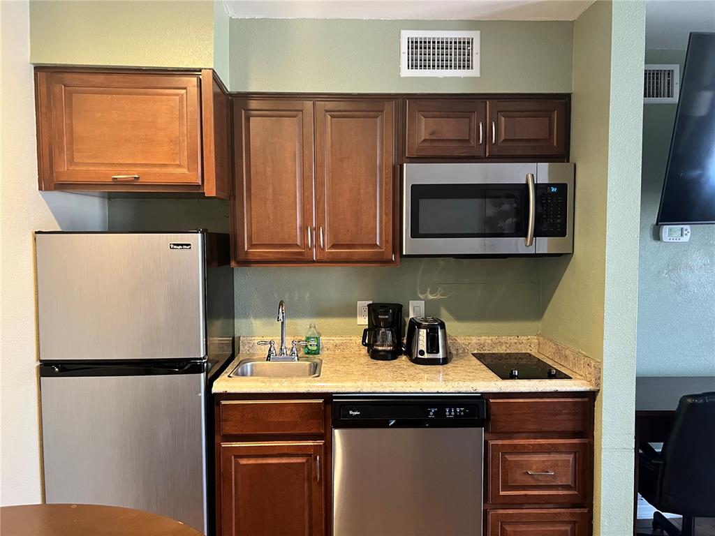 A small kitchen features dark wood cabinets, stainless steel appliances, and a granite countertop — 3100 PARKWAY BOULEVARD UNIT 611, KISSIMMEE, FL
