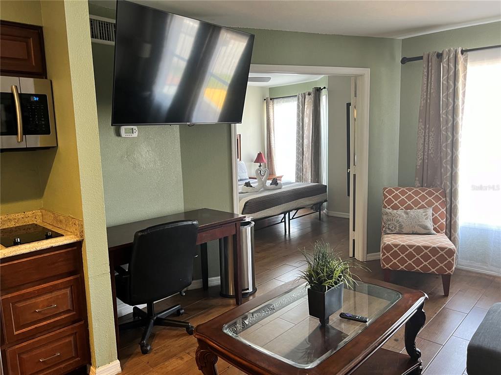 A living area with a desk, television, and coffee table opens into a bedroom — 3100 PARKWAY BOULEVARD UNIT 611, KISSIMMEE, FL