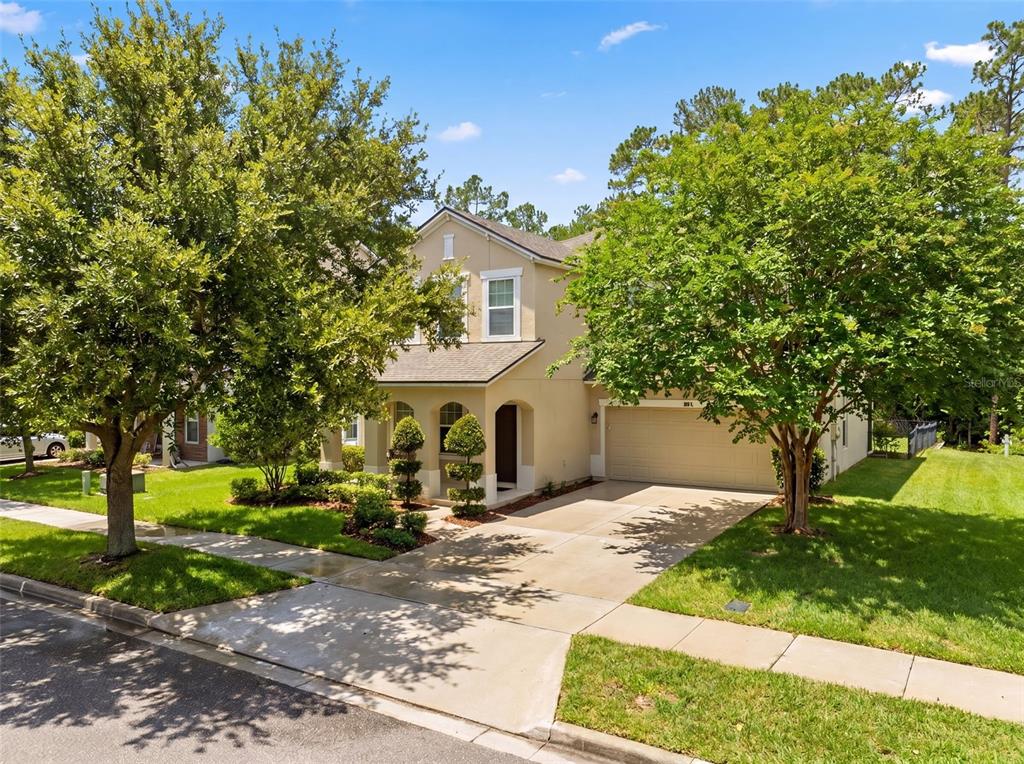 A two-story suburban house with a tan stucco exterior, a two-car garage, and mature trees — 7906 JAILENE DRIVE, WINDERMERE, FL