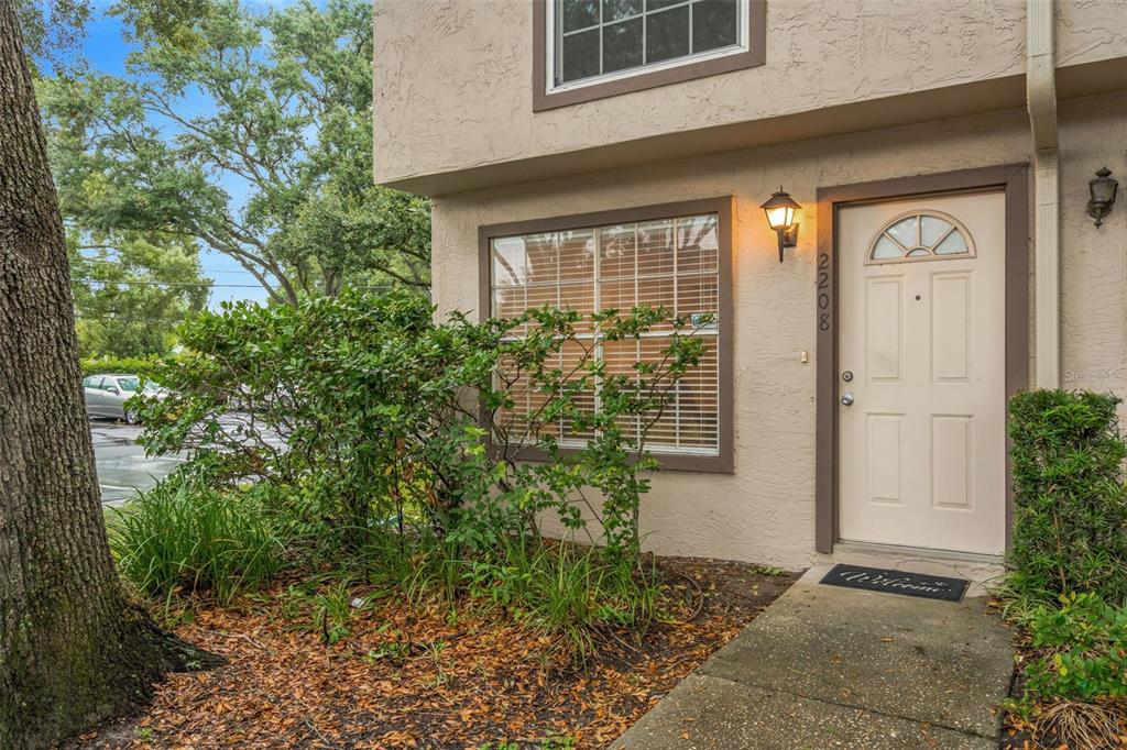 The exterior of a tan townhouse features a front door, a window, and landscaping — 2208 FLETCHERS POINT CIRCLE, TAMPA, FL