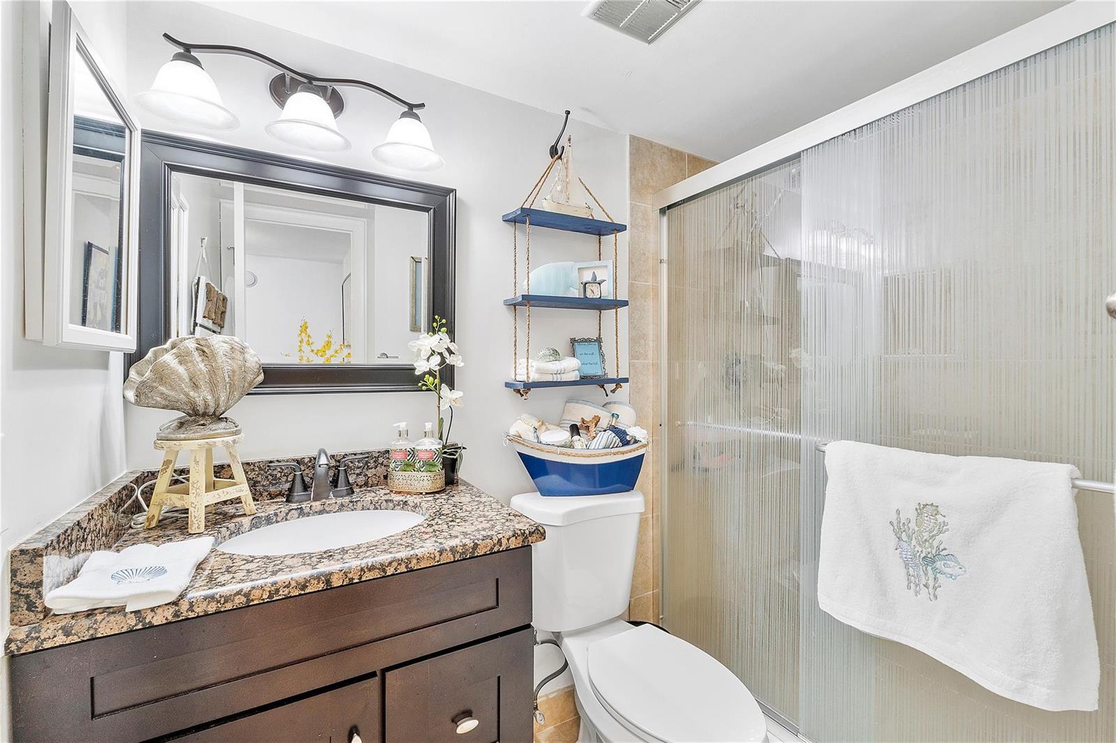 A bathroom features a dark wood vanity, granite countertop, toilet, and a glass-enclosed shower — 441 NW 76th Avenue # 101, Margate FL 33063, MARGATE, FL