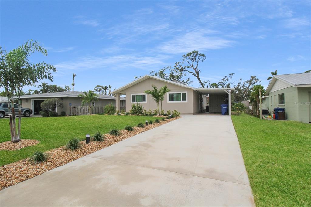 A single-story house with a concrete driveway, lawn, and landscaping under a blue sky — 5824 WILDWOOD AVENUE, SARASOTA, FL