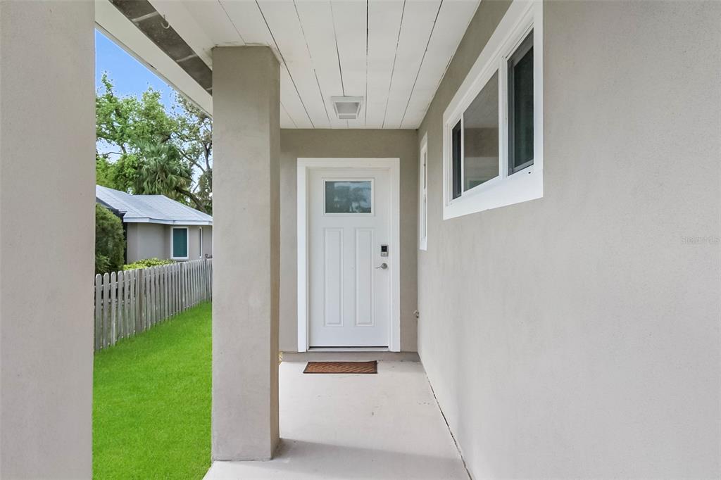 A covered concrete porch leads to a white front door with a small window — 5824 WILDWOOD AVENUE, SARASOTA, FL