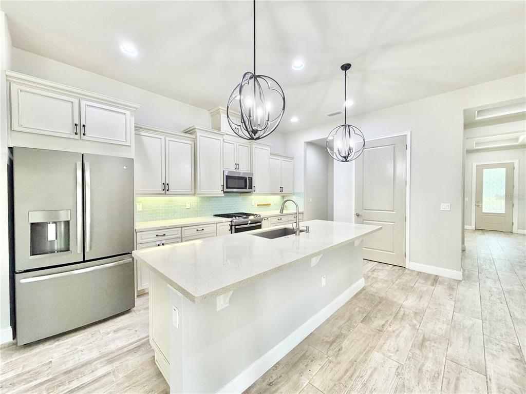 A modern kitchen features white cabinetry, stainless steel appliances, a quartz island, and pendant lighting — 11931 SW 32ND LANE, GAINESVILLE, FL