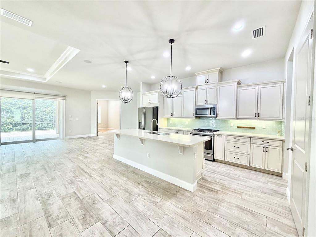 A modern kitchen features white cabinetry, a central island, and light wood-look tile flooring — 11931 SW 32ND LANE, GAINESVILLE, FL
