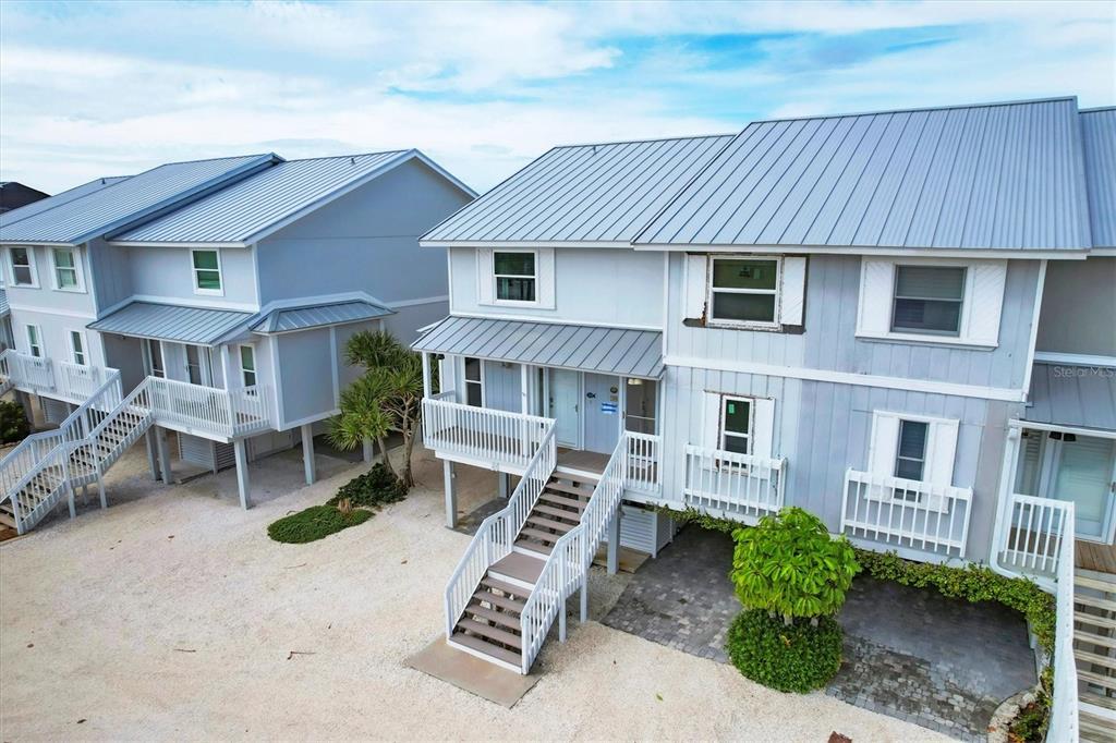 Two elevated coastal houses with metal roofs and white wooden stairs stand on a gravel lot — 420 GULF BOULEVARD UNIT 20, BOCA GRANDE, FL