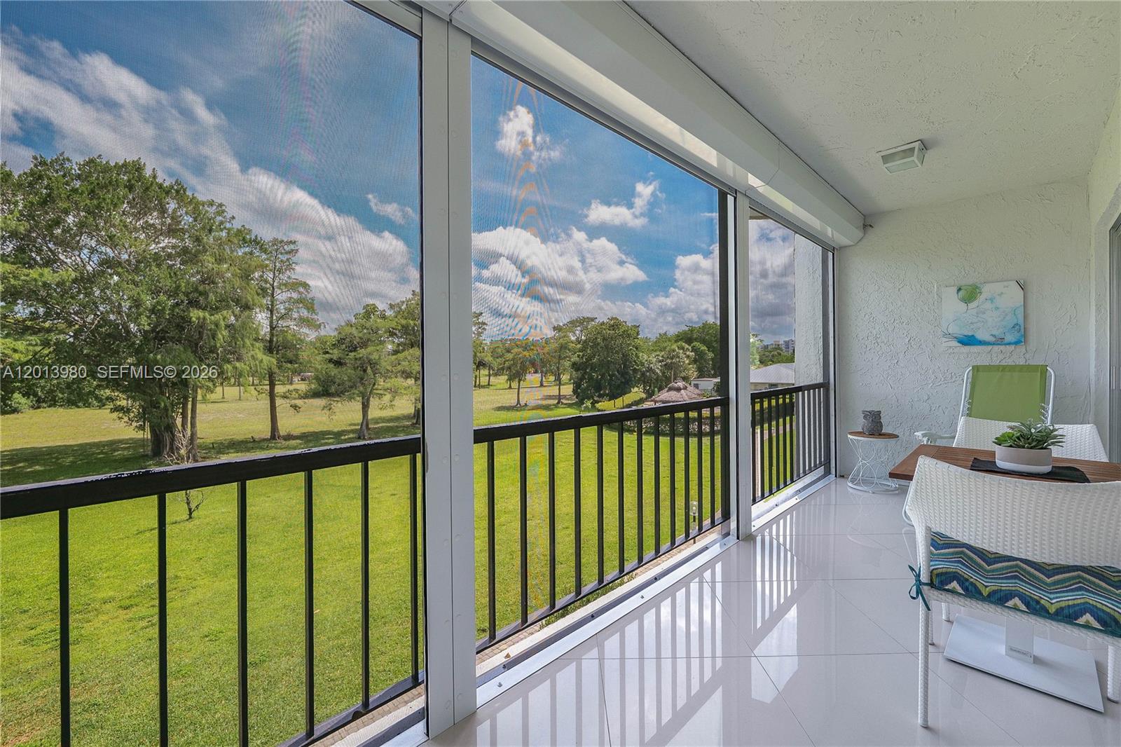 A screened-in balcony features white tile flooring, a black railing, and views of a grassy field — 6200 NW 44th St # 301, Lauderhill FL 33319, LAUDERHILL, FL