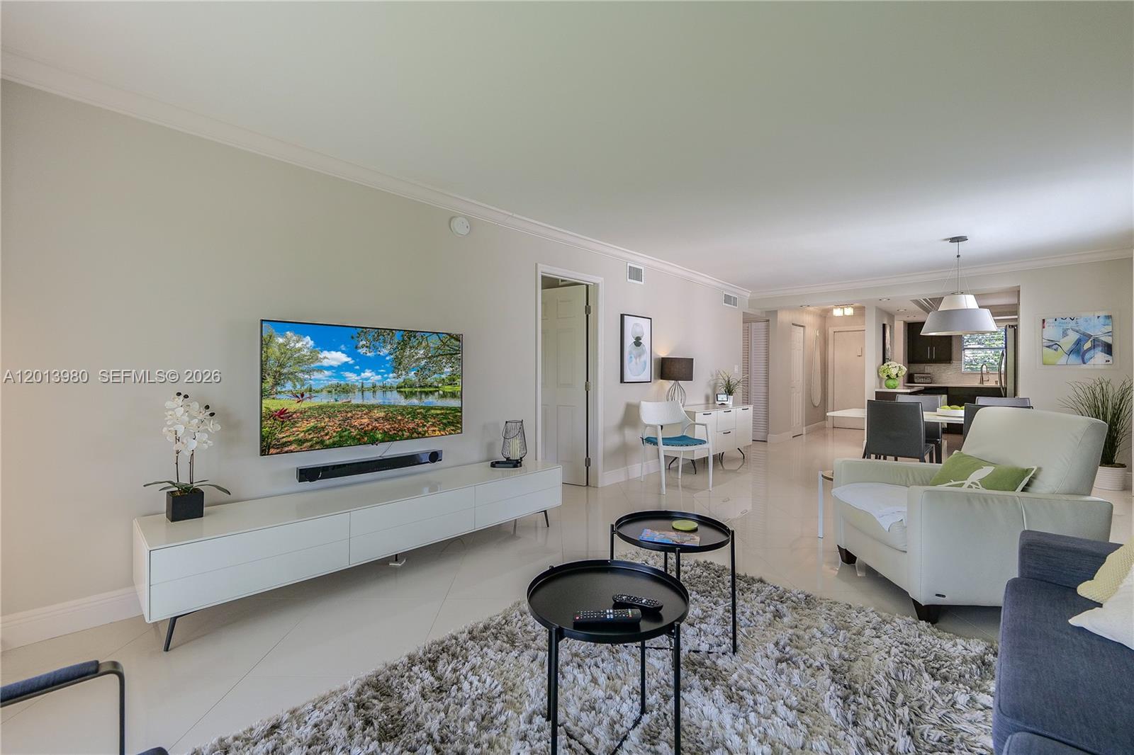 A living room features a wall-mounted television, white media console, and light tile flooring — 6200 NW 44th St # 301, Lauderhill FL 33319, LAUDERHILL, FL