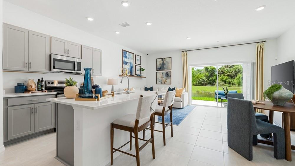 A modern open-concept kitchen and dining area with gray cabinets, white countertops, and sliding doors — 7113 PINELIT COVE, NOKOMIS, FL