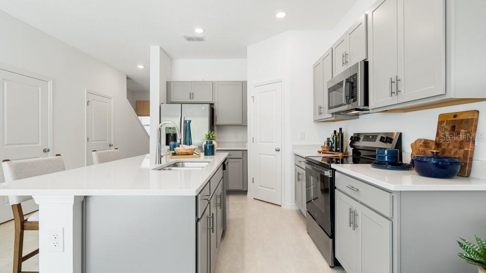 A modern kitchen features gray cabinets, white countertops, stainless steel appliances, and a central island — 7113 PINELIT COVE, NOKOMIS, FL