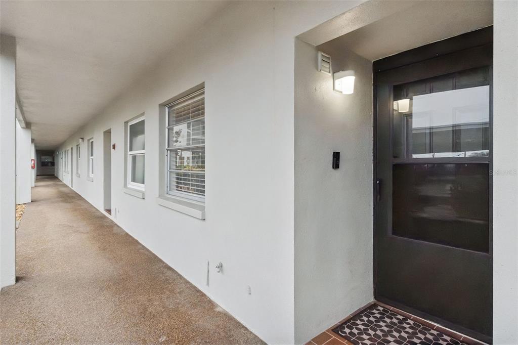 An exterior walkway leads past several apartment doors and windows toward a dark front door — 5157 SILENT LOOP UNIT 110, NEW PORT RICHEY, FL