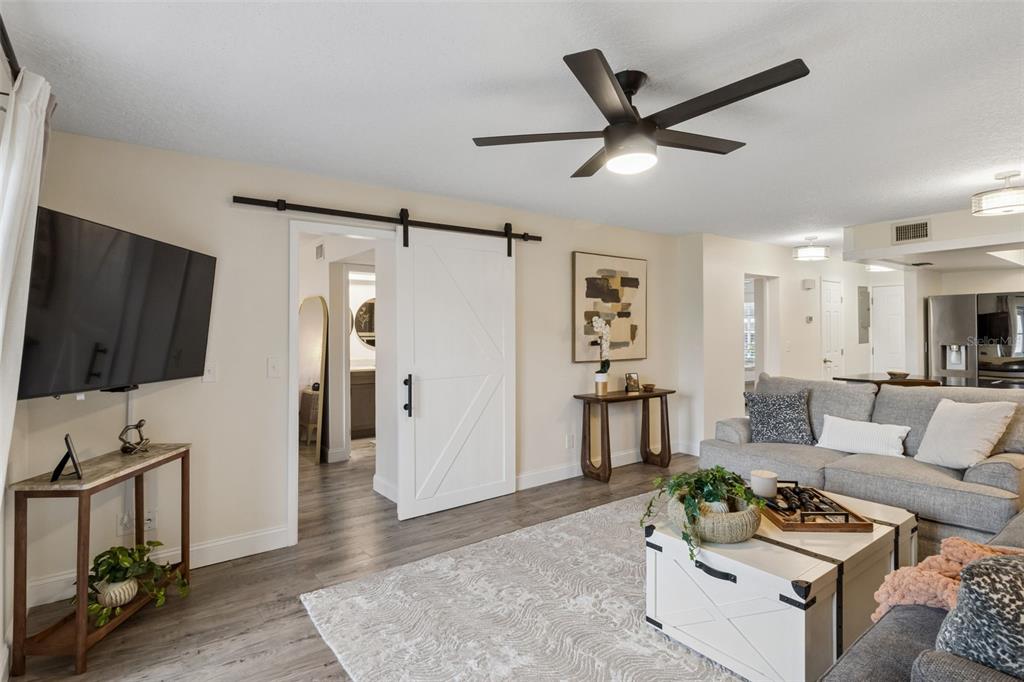 A living room features a white barn door, gray flooring, a ceiling fan, and a sofa — 5157 SILENT LOOP UNIT 110, NEW PORT RICHEY, FL