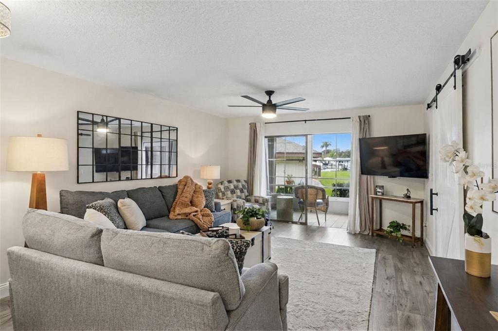 A living room features a gray sectional sofa, a wall mirror, and a sliding glass door — 5157 SILENT LOOP UNIT 110, NEW PORT RICHEY, FL