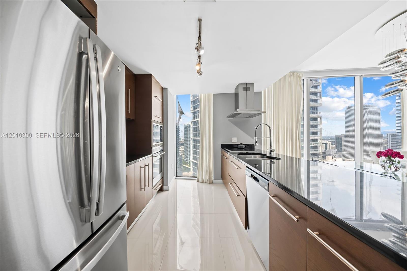 A modern kitchen features wood cabinets, stainless steel appliances, and floor-to-ceiling windows with city views — 495 Brickell Ave # 3710, Miami FL 33131, MIAMI, FL