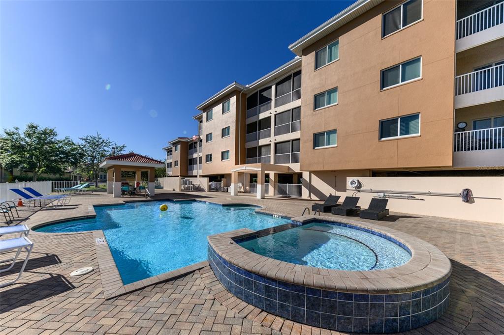 An outdoor swimming pool and hot tub are situated in front of a multi-story apartment building — 3322 PURPLE MARTIN DRIVE UNIT 135, PUNTA GORDA, FL