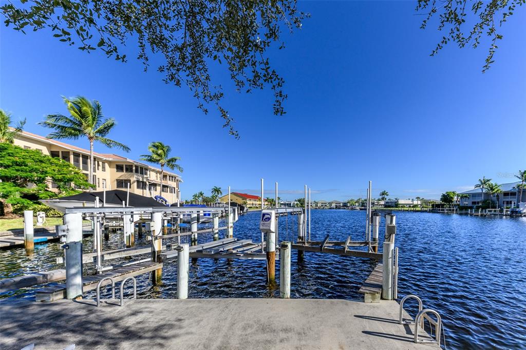 A concrete boat dock with a lift extends into a canal lined with residential buildings — 3322 PURPLE MARTIN DRIVE UNIT 135, PUNTA GORDA, FL