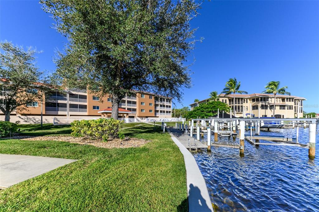 A waterfront view of a multi-story apartment building with a boat dock and lawn — 3322 PURPLE MARTIN DRIVE UNIT 135, PUNTA GORDA, FL