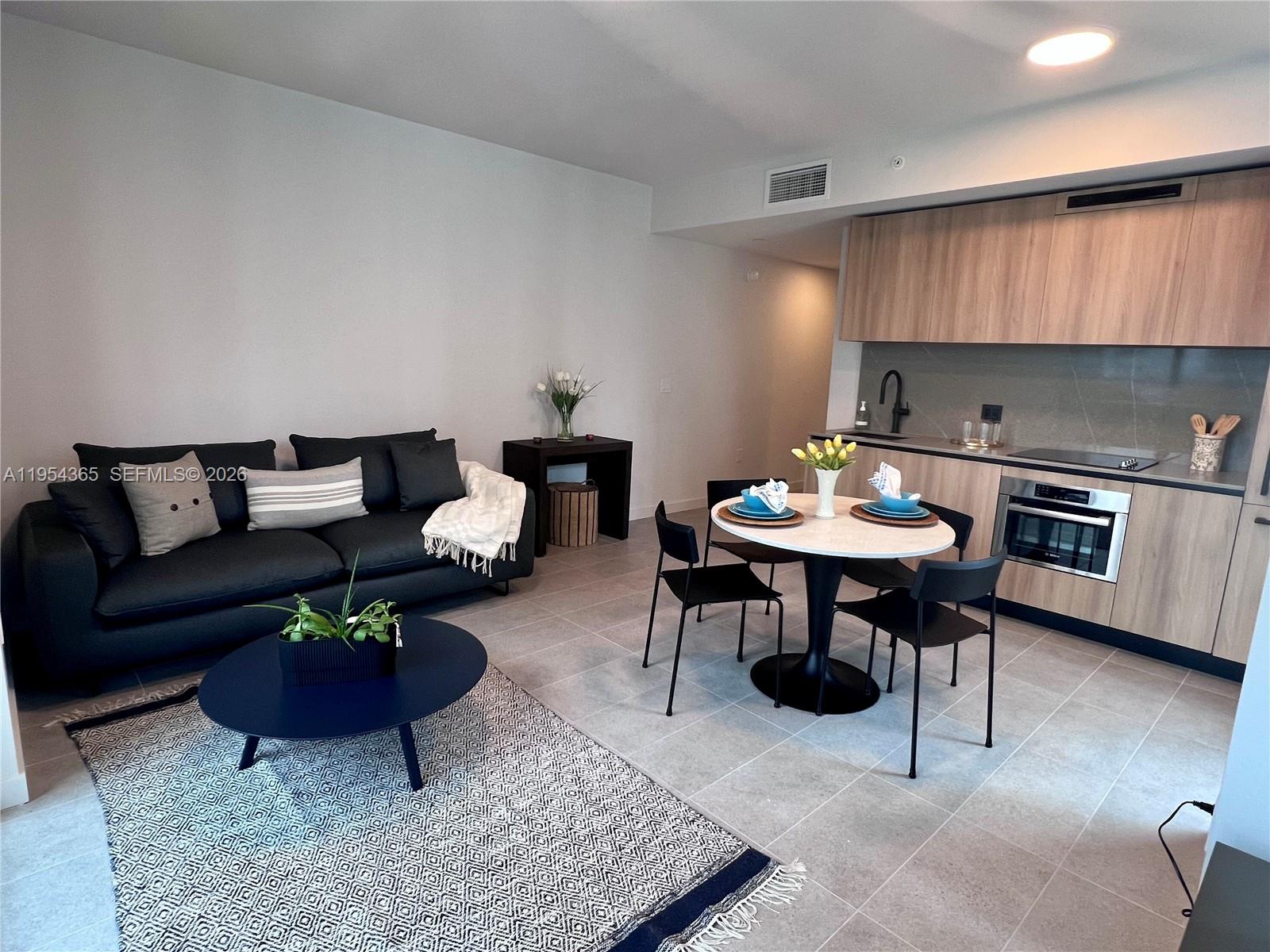 A modern open-concept living room and kitchen area with light tile flooring and wood cabinetry — 121 NE 5th St # 1608, Miami FL 33143, MIAMI, FL
