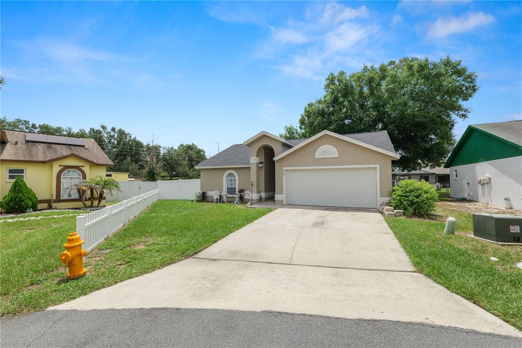 A tan single-story house with a two-car garage, concrete driveway, and a white picket fence — 6201 VINTAGE DRIVE, LAKELAND, FL