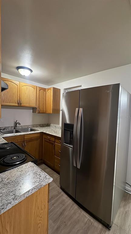 A kitchen features wood cabinets, granite countertops, a stainless steel refrigerator, and light wood flooring — 3775 SW 147TH LANE ROAD, OCALA, FL