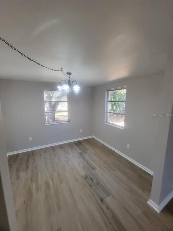 An empty room with light wood-look flooring, gray walls, two windows, and a hanging chandelier — 3775 SW 147TH LANE ROAD, OCALA, FL