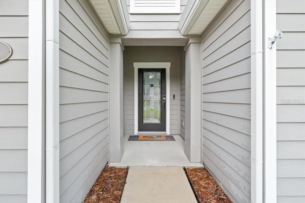 A concrete walkway leads to a front door with a glass panel under a porch — 27 COLORADO SPRINGS WAY, ST AUGUSTINE, FL