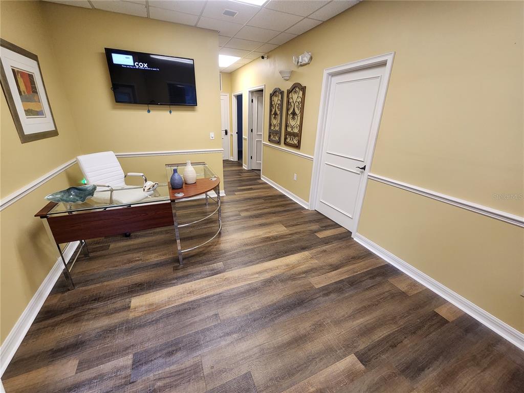 An office space features a glass desk, wood-look flooring, and a wall-mounted television — 101 NW 75TH STREET UNIT Suite 1-A, GAINESVILLE, FL