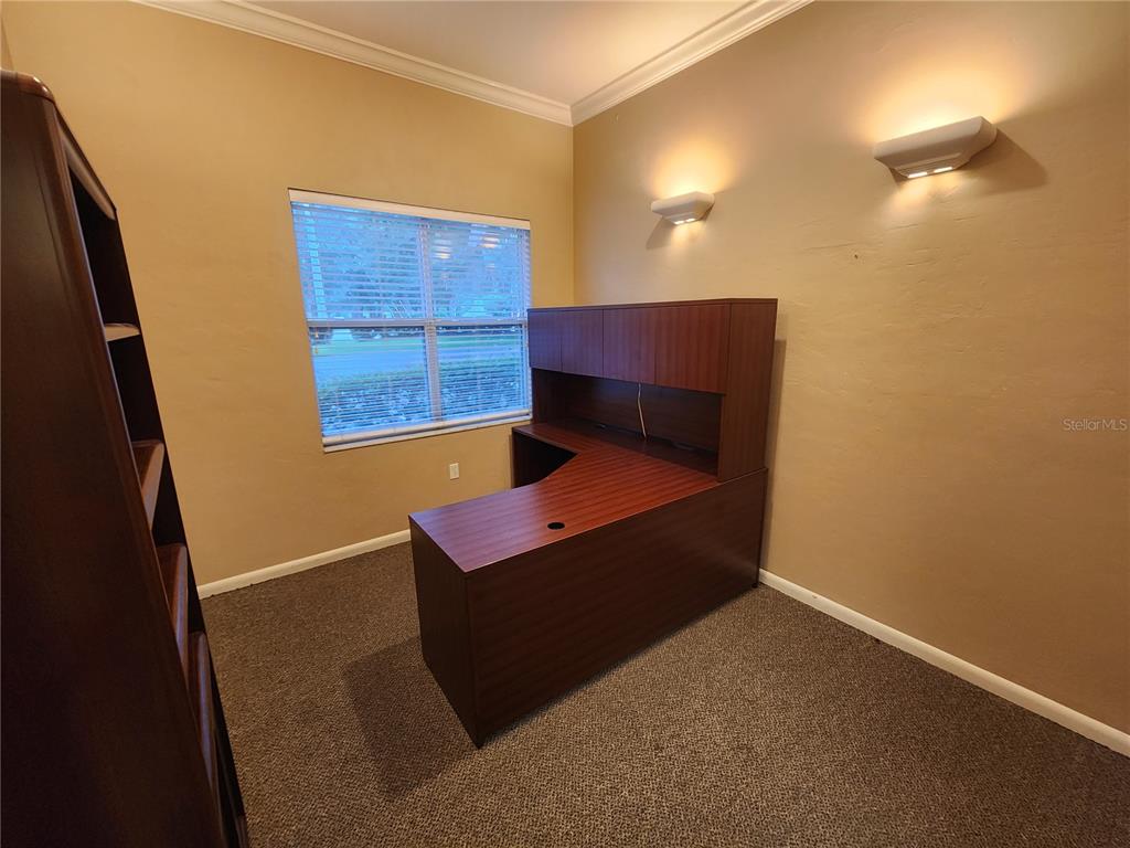 A home office features a dark wood L-shaped desk, beige walls, and carpeted flooring — 101 NW 75TH STREET UNIT Suite 1-A, GAINESVILLE, FL