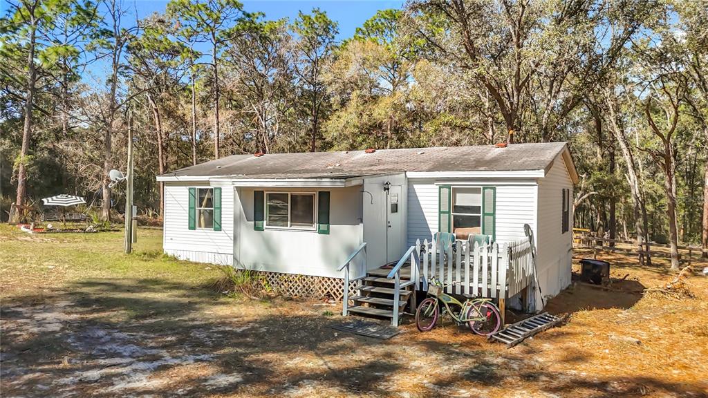 A white single-wide mobile home sits in a wooded lot with a small front deck — 6421 SUNNYSIDE RANCH ROAD, BROOKSVILLE, FL