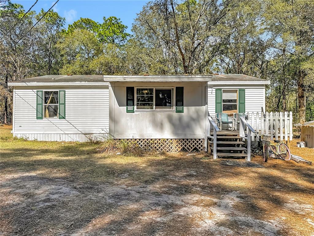 A single-story mobile home with white siding, green shutters, and a wooden front porch — 6421 SUNNYSIDE RANCH ROAD, BROOKSVILLE, FL
