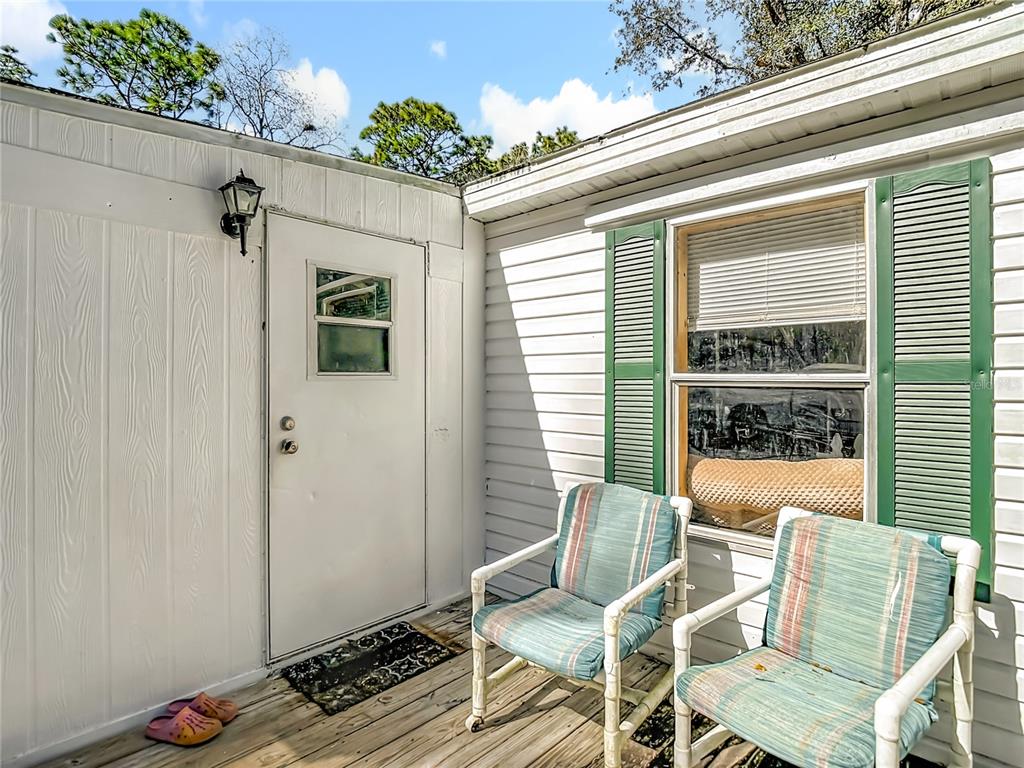 A wooden deck features two chairs, a white door, and a window with green shutters — 6421 SUNNYSIDE RANCH ROAD, BROOKSVILLE, FL
