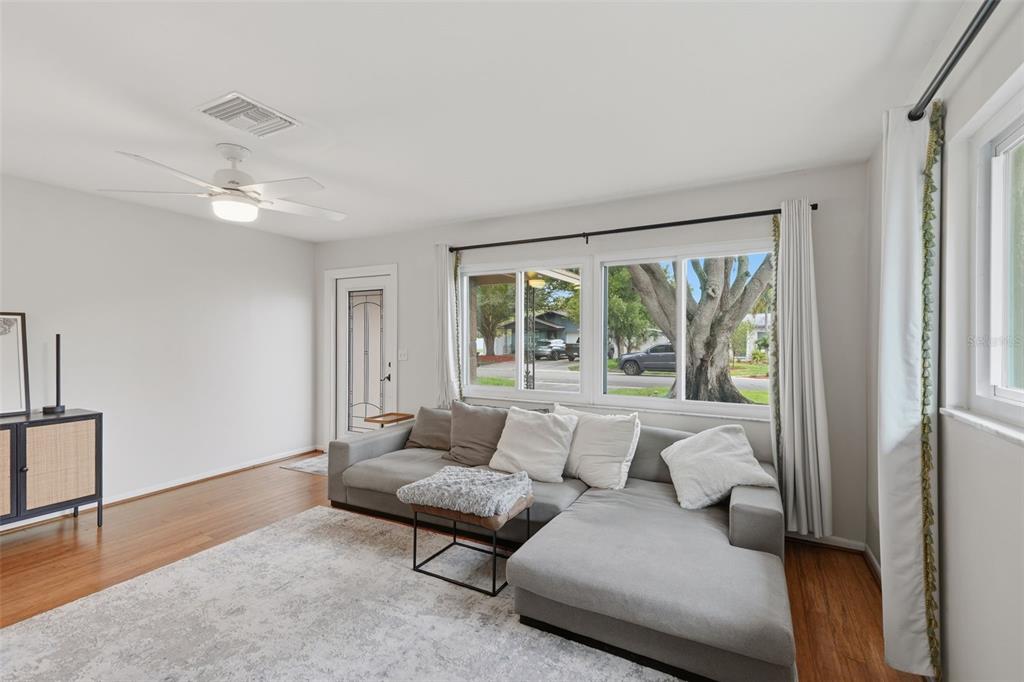 A living room features a grey sectional sofa, hardwood floors, and a large window — 205 SE MONROE CIRCLE N, ST PETERSBURG, FL