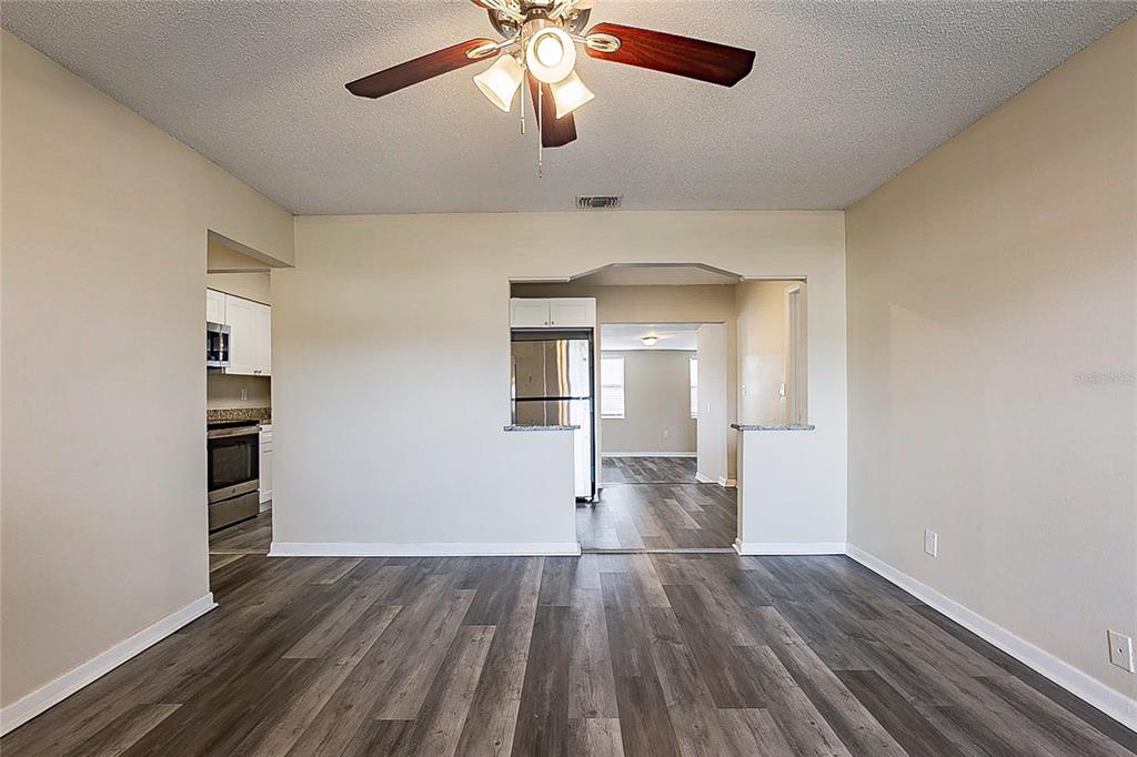 A living area with wood-look flooring, a ceiling fan, and an opening to the kitchen — 8528 GOLD RIDGE CIRCLE, TAMPA, FL