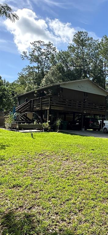 A two-story house with a large wooden deck stands on stilts above a grassy yard — 7035 SE 23RD COURT, OCALA, FL