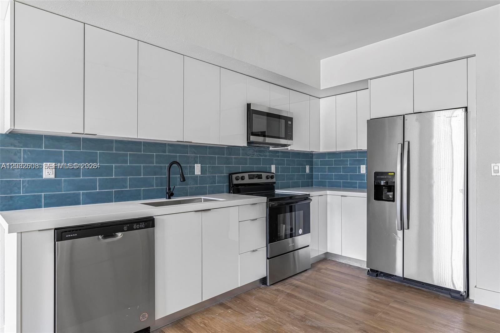 A modern kitchen features white flat-panel cabinets, stainless steel appliances, and a blue subway tile backsplash — 16955 SW 100th Ave # 1, Miami FL 33157, MIAMI, FL